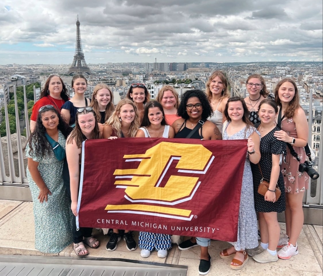 Study Abroad students in Paris posing for a picture with a CMU flag, and an Eiffel Tower in the background.