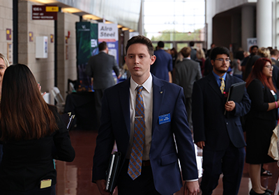 A male student in a blue blazer walking down the hallway during a career fair.