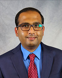 Headshot of Abdullah Islam wearing a blue suit with a blue shirt and a red necktie.