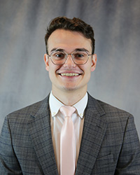 Headshot of Nathaniel Riggan wearing a grey blazer, white shirt, and pink tie.