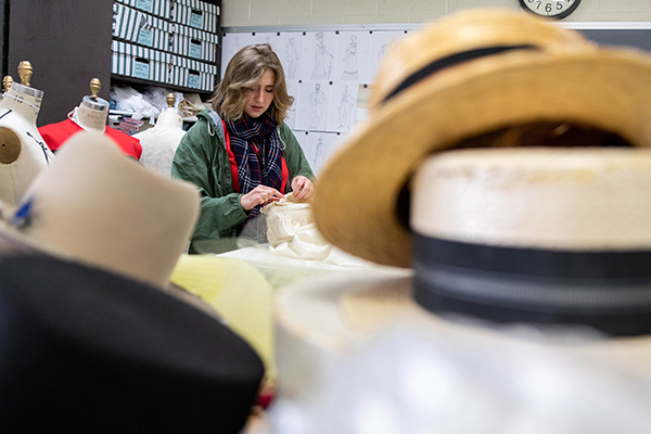 A female student working in costume department with hats and other designs.
