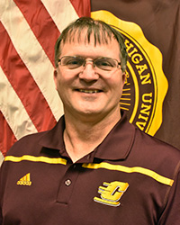 Randy Wright stands in front of a United States flag and Central Michigan University flag