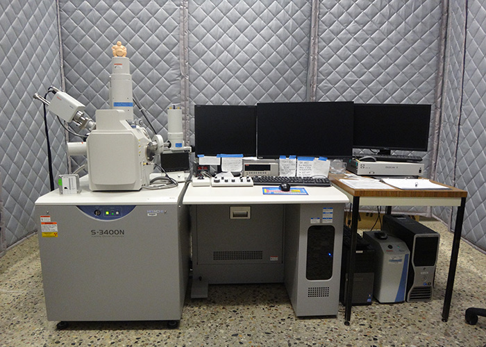 The Hitachi 3400 Scanning Electron Microscope next to a desk with multiple computer screens in the microscopy lab.
