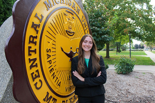 Lauren Dey in a green shirt and black jacket in front of the CMU Seal.