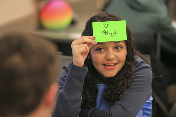 Student in an active classroom with a chemical formula on her head.