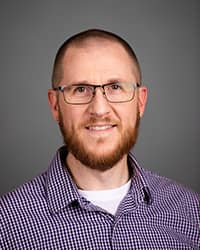 Nathan Dean, Counselor, professional headshot picture, wearing a checkered button down shirt, and glasses with a grey background