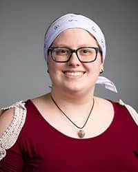 Wenda Dexter, Counseling Center Intern profile picture. Wearing glasses, a maroon shirt and white headband with a dark grey background.