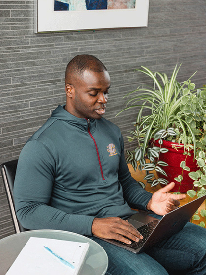 Online-Campus-Everyday-Essential-Resources-480x720 Man in CMU sweater working on his computer with a notebook and pen
