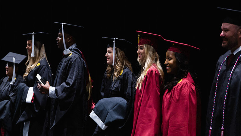 Seven students in graduation gowns and caps standing on stage