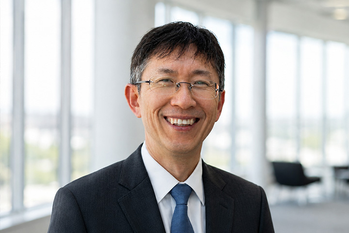 Portrait of accounting professor Keejae Hong smiling in a black suit and blue tie with a blurred office background.