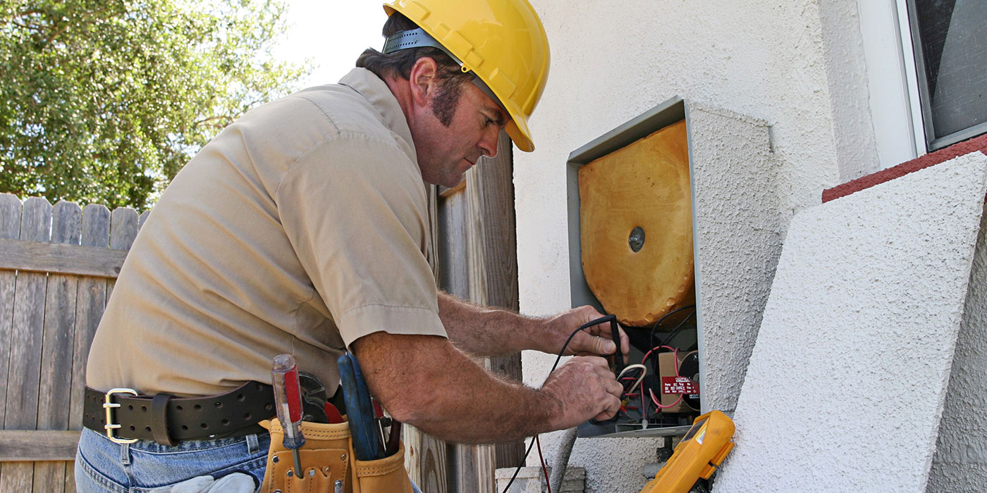 A man in a yellow hard hat works on an HVAC system outside a building.