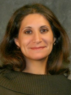 Professional headshot of Luba Fishman in green attire against a gray background.
