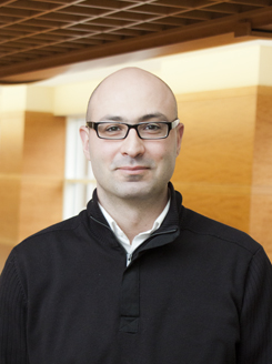 Imad Haidar wears a black jacket and a button up shirt while looking at the camera.