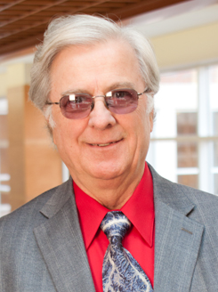 Jim Mentele wears a grey suit with a red button up shirt while looking at the camera.