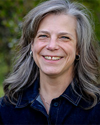 Professional headshot of a woman in dark blue jean jackets against a green background