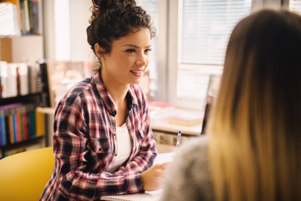 A female student wearing a red flannel shirt sitting with a librarian discussing research.