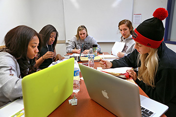 Five students work on a laptops at a table in group study room.