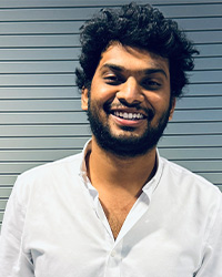 Still photo of graduating student Si Teja Puli in a white collared button shirt against a striped background