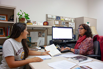 A librarian in front of a computer gives a consultation to student, who sits across a desk.
