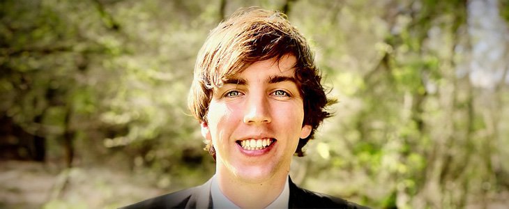 Headshot of Lee Parker in a dark suit with white collar shirt against a green brushy background