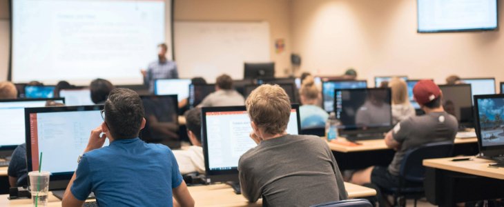 Students facing towards the front of the classroom paying attention to the professor at the front.