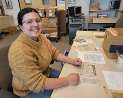 Clarke Historical Library Student Employee Natalie wearing a mustard yellow long sleeve sorting through documents to be archived