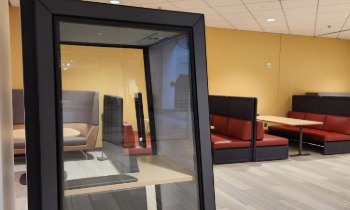 a glass phone booth with a table and chairs behind it