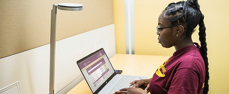 Student in maroon shirt at a laptop using Libraries Smart Search