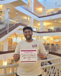 a smiling man holding a sign that says, Thank you. Because of you I can achieve my academic goals without worries.