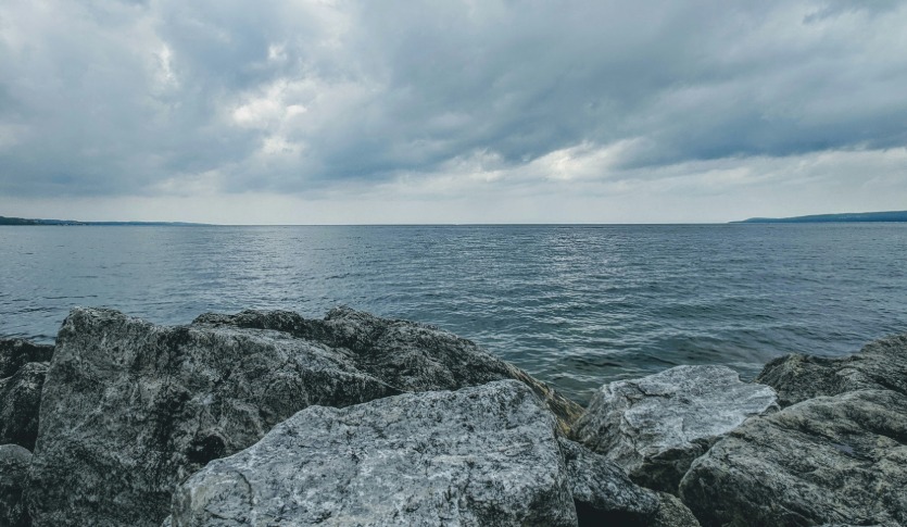 Image of dark water on a gloomy overcast day with large grey rocks in the forefront.