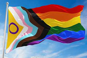 LGBT Progress Pride Flag on a flag pole blowing in the breeze with blue sky.