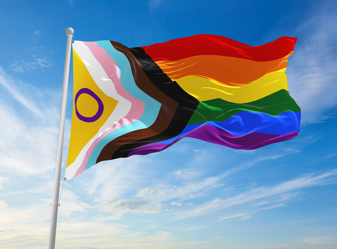 LGBT Progress Pride Flag on a flag pole blowing in the breeze with blue sky.