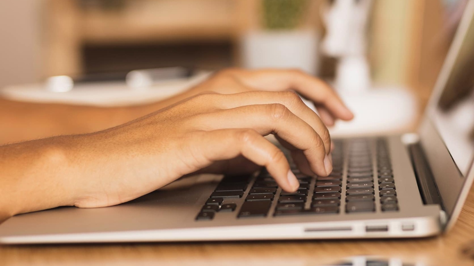 Side profile of hands typing on a Macbook keyboard.