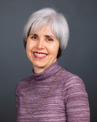 Alejandra Rengifo head and shoulders portrait, smiling, with a gray background