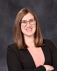 Erika Zambarano portrait, showing head and shoulders, smiling, on a gray background