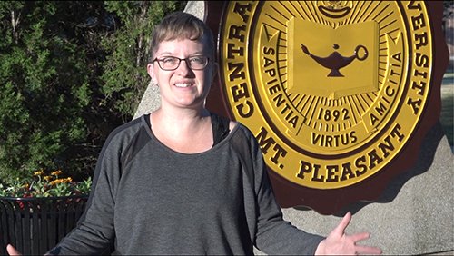 An instructor is recorded giving a presentation outdoors in front of the University Seal on Warriner Mall.