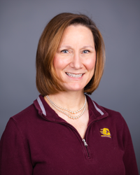 A portrait of Kirsten Nicholson showing head and shoulders, smiling, on a gray background.