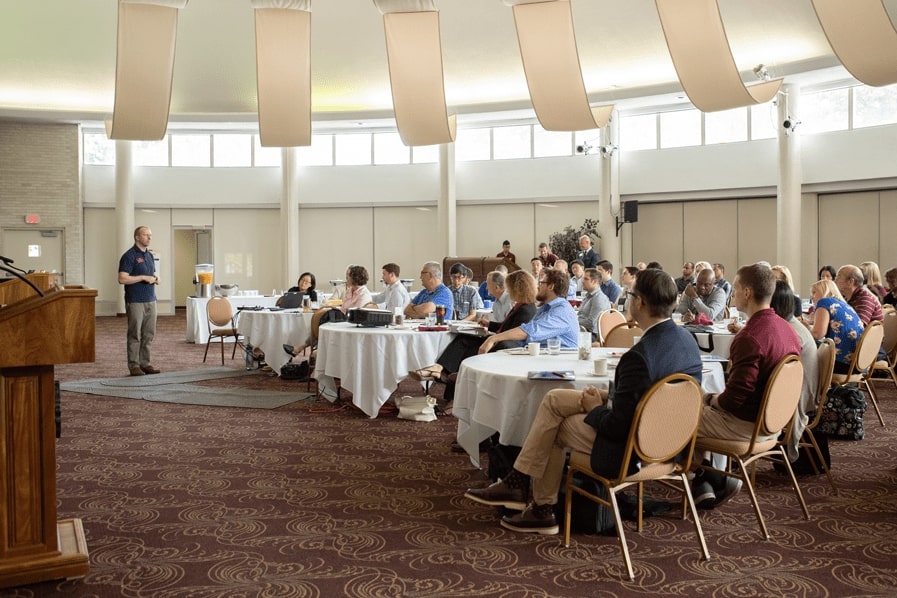 Audience seated at round tables listening to a speaker in the Bovee UC Rotunda