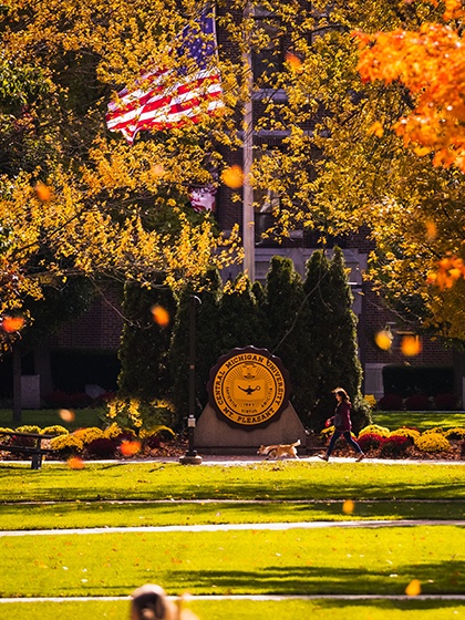 A woman walking a dog in front of the Central Michigan University seal.