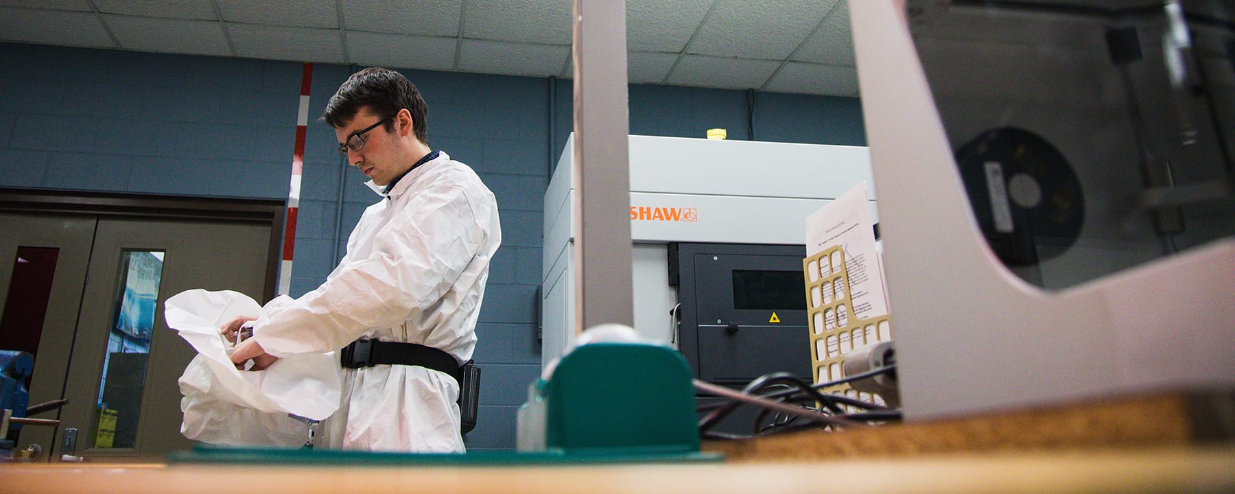 A young man in a biohazard suit stands in a lab.