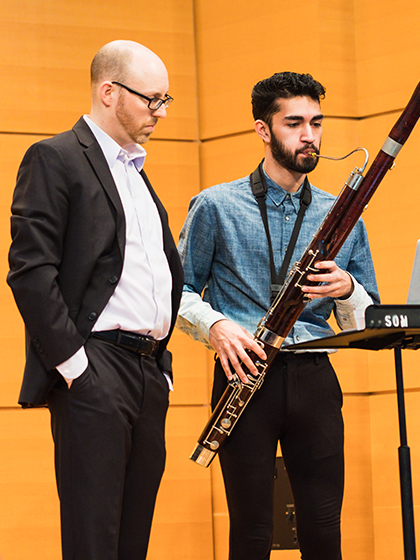 A professor stands next to an honors student playing the bassoon.