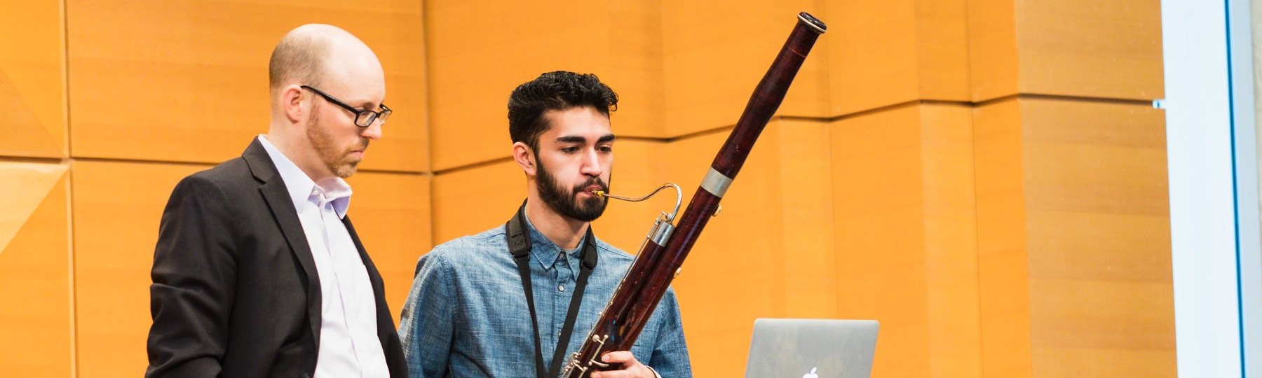 A professor stands next to an honors student playing the bassoon.