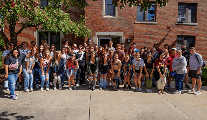 Group of students standing outdoors in front of a brick building.