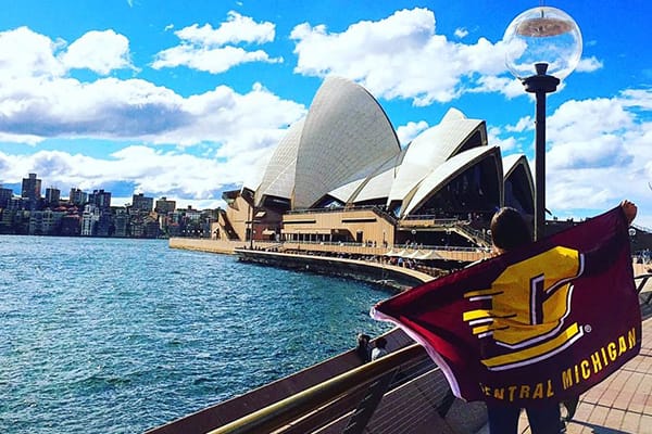 A student holding a CMU flag by the Sydney Opera House in Australia.