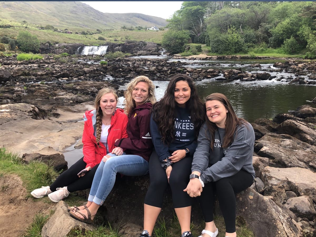 Students pose by rocks and a waterfall in Ireland while studying abroad.