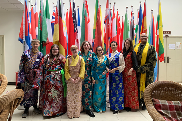 Eight people in traditional attire standing in front of national flags.
