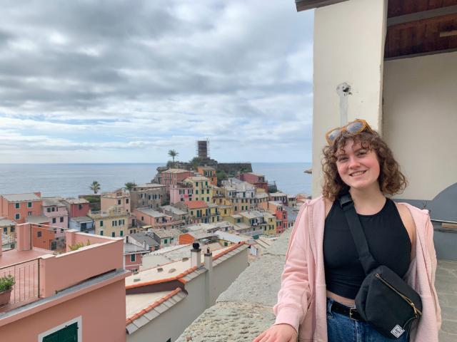 Student looking forward with Italian coastline and colorful buildings scattered behind her.