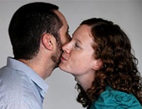 A man and a woman greeting each other with a side kiss near the cheek.