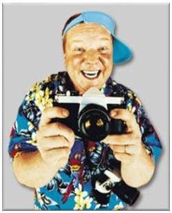 A man wearing a blue Hawaiian shirt while holding a camera.