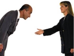 A stock photo of a man bowing and a woman holding out her hand for a handshake.